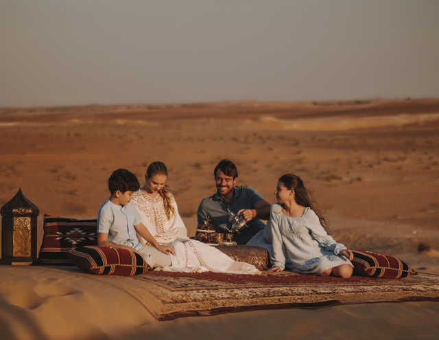 Family enjoying Bedouin tea in the desert near Aldhafra Resort, surrounded by traditional setup.