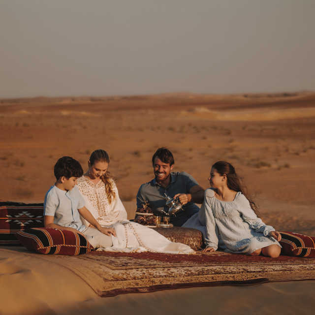 Family enjoying Bedouin tea in the desert near Aldhafra Resort, surrounded by traditional setup.